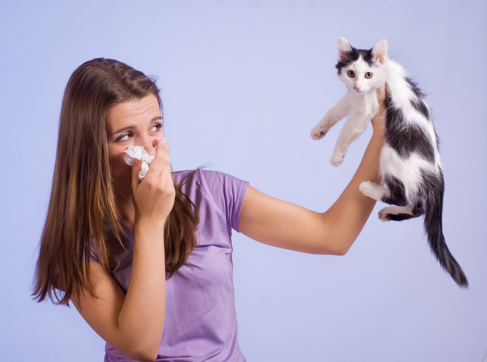 a woman covering her nose with one hand and holding a cat with the other