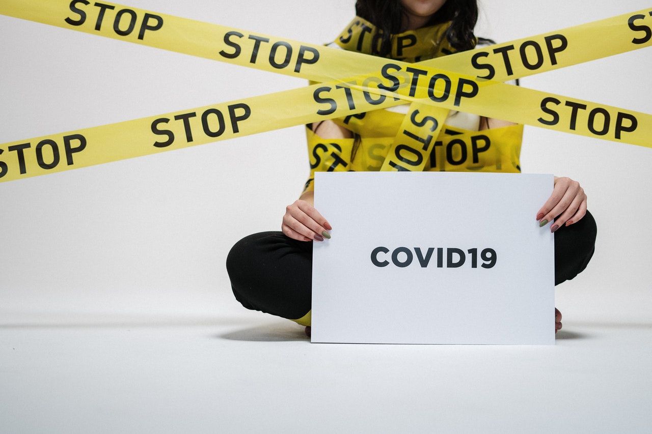 a teenager sitting on the floor wrapped with police tape the girl is holding a covid 19 banner