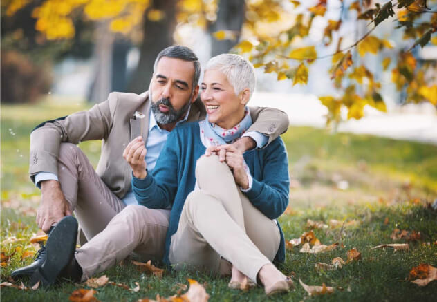 middle age couple smiling while holding a dandelion sitting on the grass
